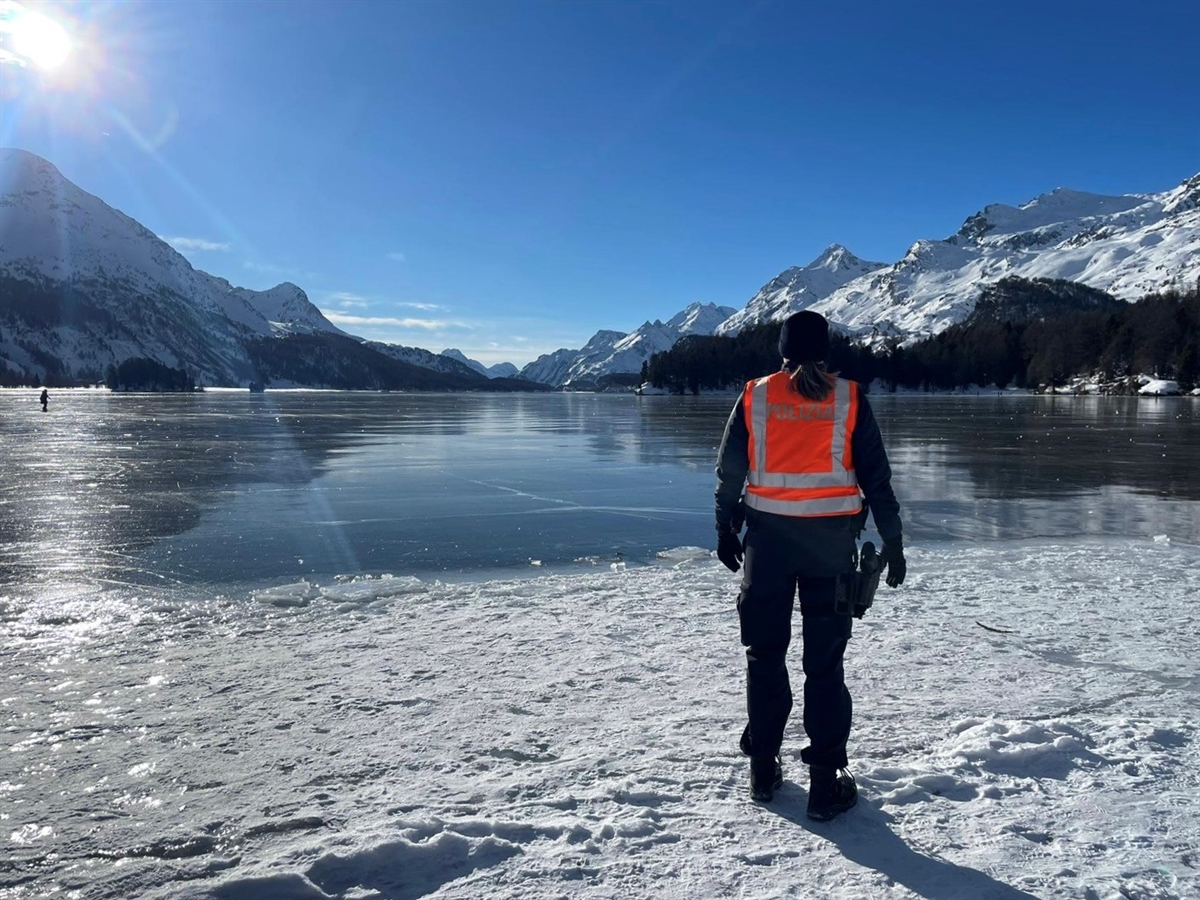 Rechts eine Polizistin die auf den grösstenteils gefrorenen Silsersee schaut. Im Hintergrund Berge und strahlendes Winterwetter.