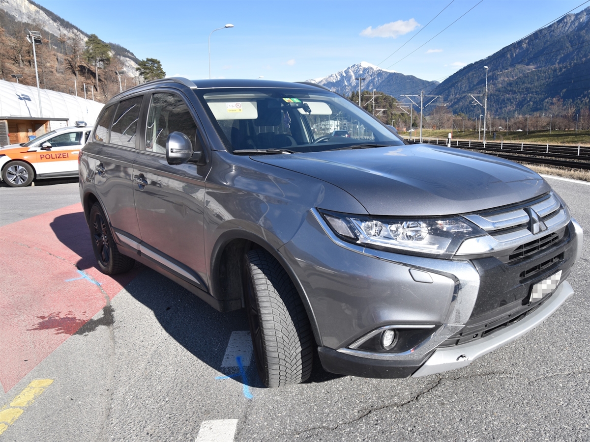 Das schräg im Verzweigungsbereich stehende Auto. Der Radweg ist mit roter Farbe eingefärbt. Im Hintergrund ein Polizeiauto, Berge und heiterer Himmel.