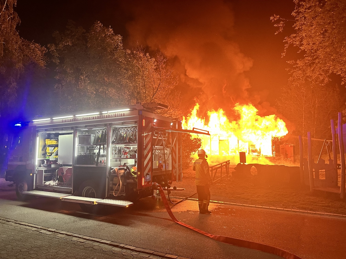 Feuerwehrfahrzeug im Einsatz, Holzscheune im Vollbrand im Hintergrund