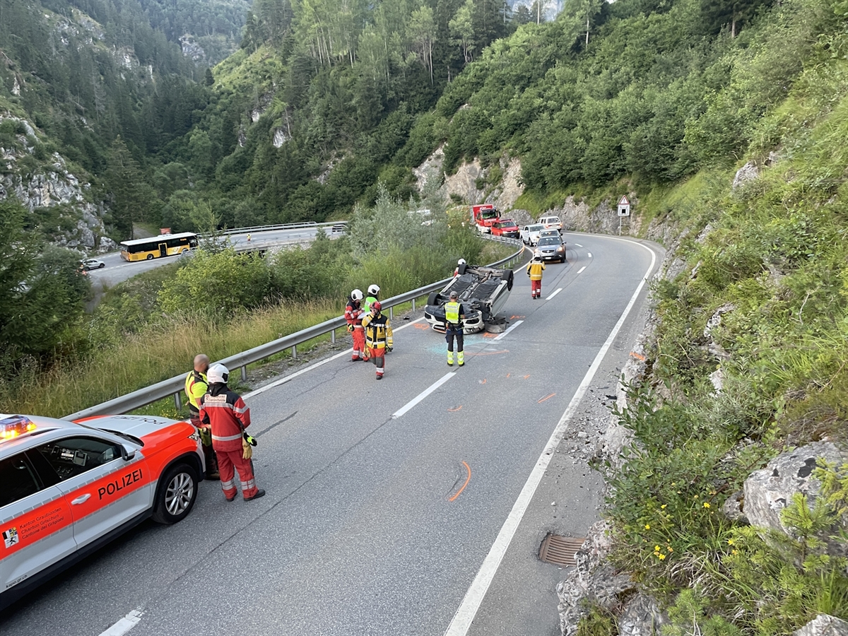 Links ein Polizeiauto. Rechts davon Rettungskräfte der Feuerwehr und das auf dem Dach liegende Auto.