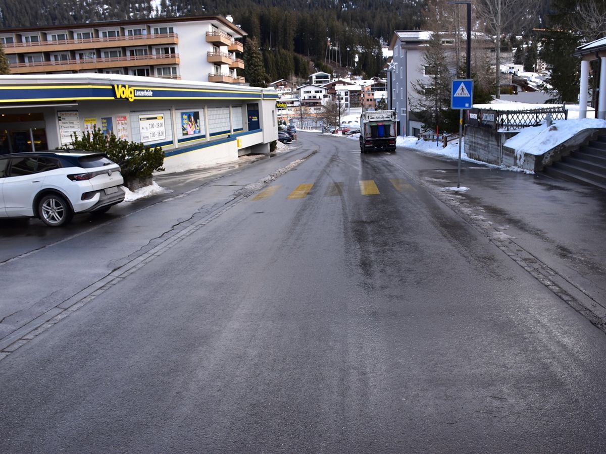 Links neben der Voa Sporz das Trottoir und gleich anschliessend das Unfallauto. Weiter befindet sich auf der linken Seite ein Lebensmittelgeschäft.
