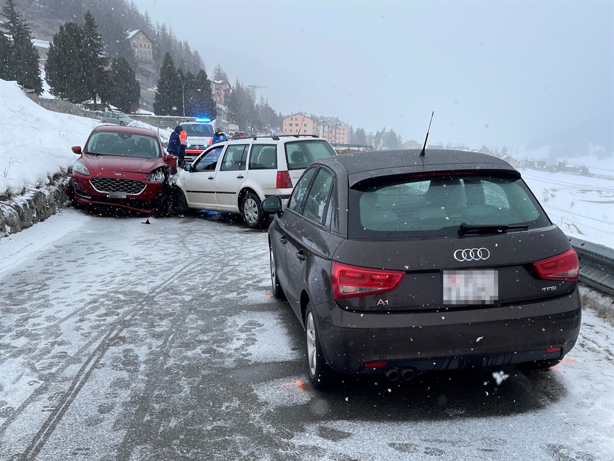 Die drei Unfallfahrzeuge stehen auf der schneebedeckten Nebenstrasse vor Zuoz. Im Hintergrund zwei Personen, ein Polizist sowie ein Polizeifahrzeug. Es herrscht leichter Schneefall.