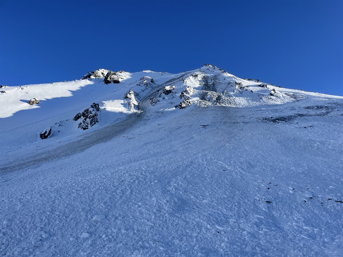 Blauer Himmel mit Berggipfel und Lawinenhang
