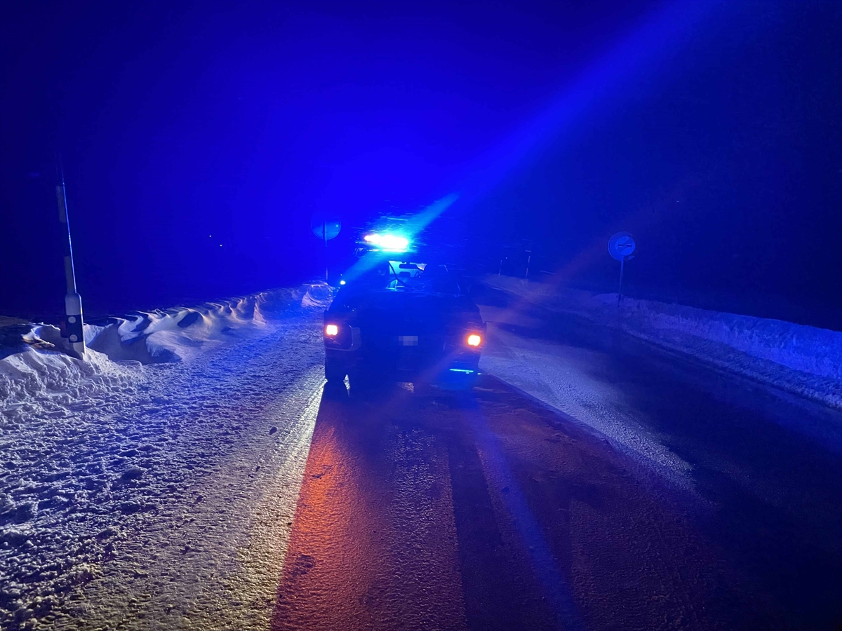 Verschneite und vereiste Fahrbahn. Mitten im Foto der am Verkehrsunfall beteiligte Personenwagen und im Hintergrund das leuchtende Blaulicht.