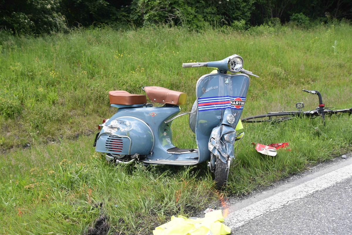 Der total beschädigte blaue Roller, eine Vespa, steht auf der Wiese beim Strassenrand.