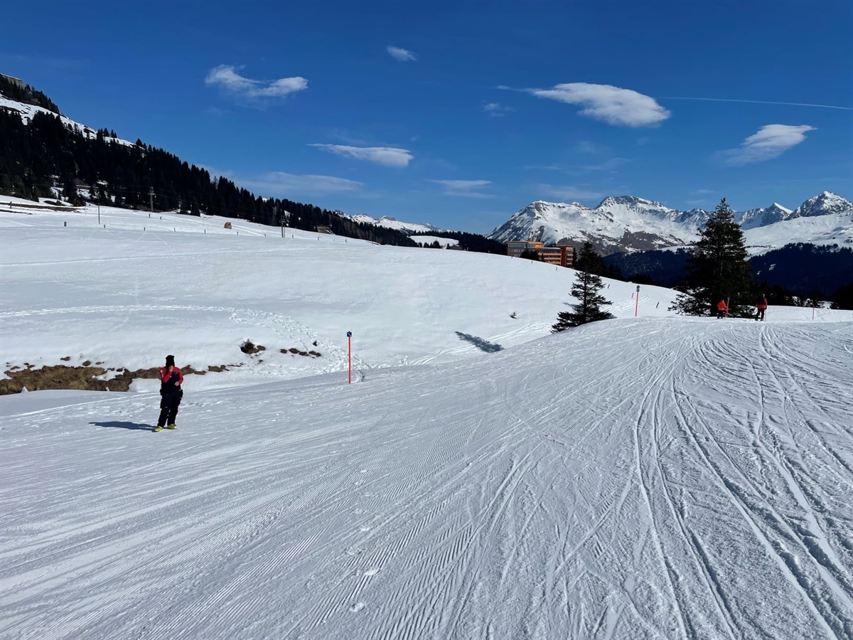 Die Skipiste an deren Ende der Verunfallte in ein Bachbett stürzte. Im Hintergrund Berge und heiterer Himmel.