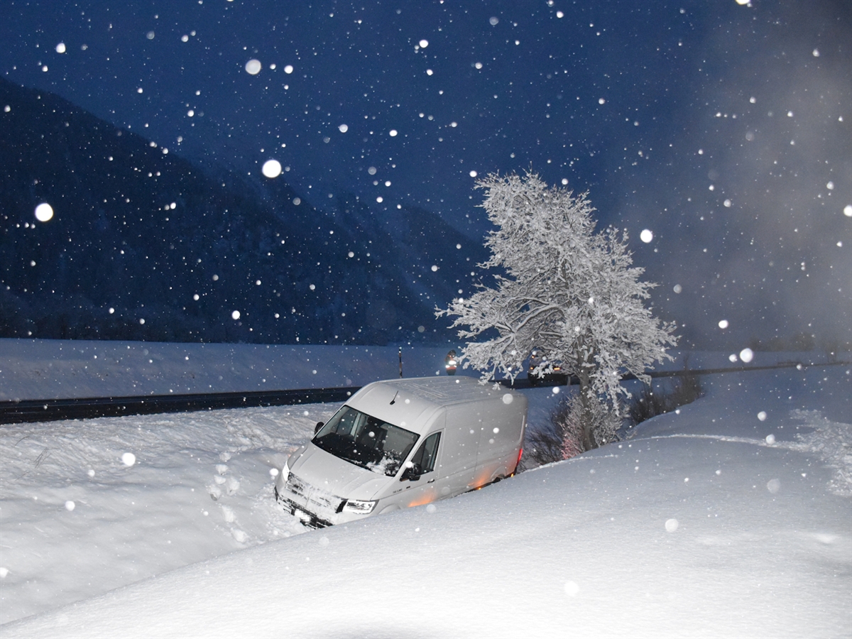 Der Lieferwagen liegt neben der Strasse angrenzend am Flusswuhr des Inns. Der Schneefall wird durch den Blitz des Fotoapparates erhellt. Die Landschaft ist tief verschneit.