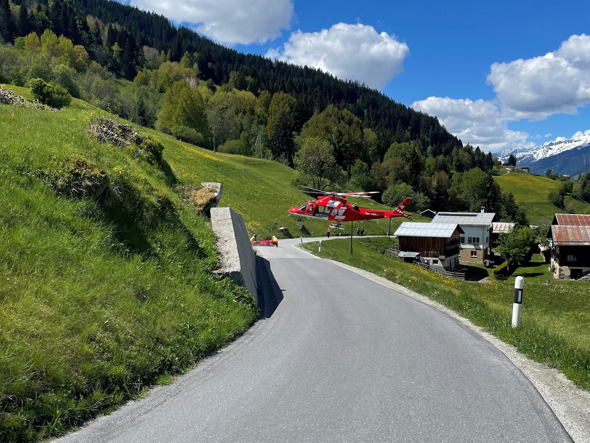 Die Kurvenkombination mit dem landenden Heli. Auf der Fahrbahn sind Flughelfer und Notarzt bereit, den Patienten in den Heli einzuladen. Das saftige Grün der Wiesen wird mit malerisch blauem Himmel ergänzt