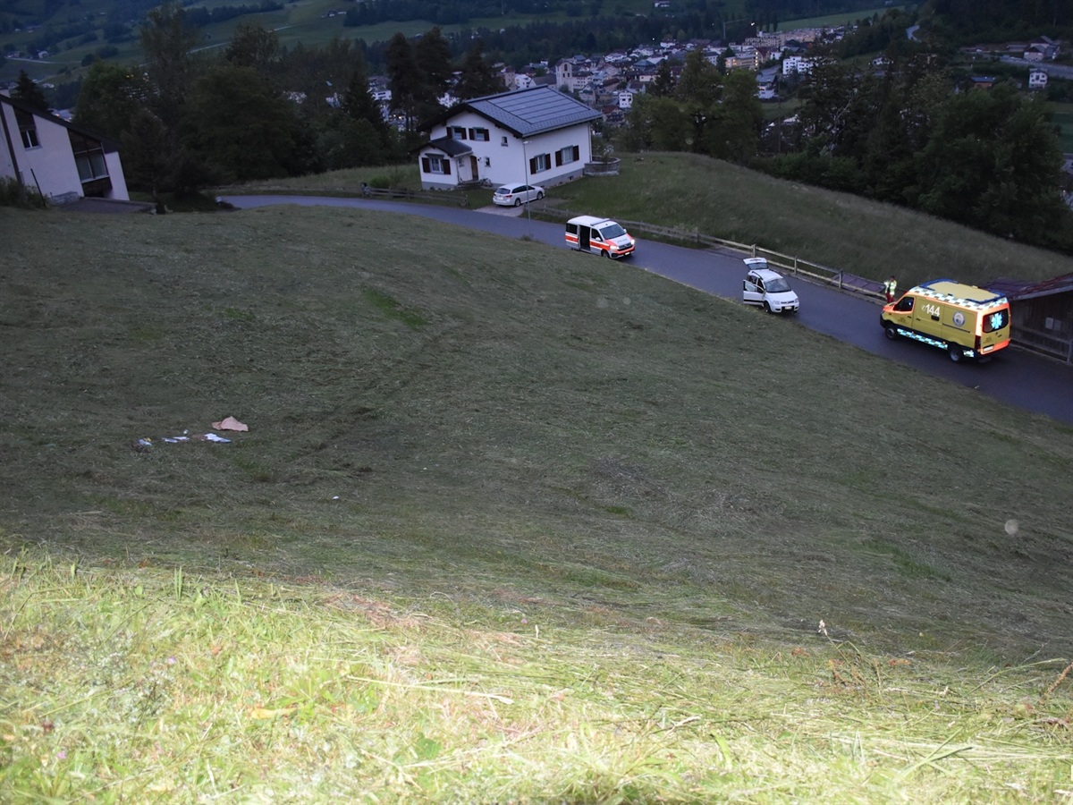 Das talwärts abfallende Wiesland, über welches sich das Auto mehrmals überschlug. Am Wieslandende die Strasse mit Unfallauto, Polizeiauto und Rettungswagen.