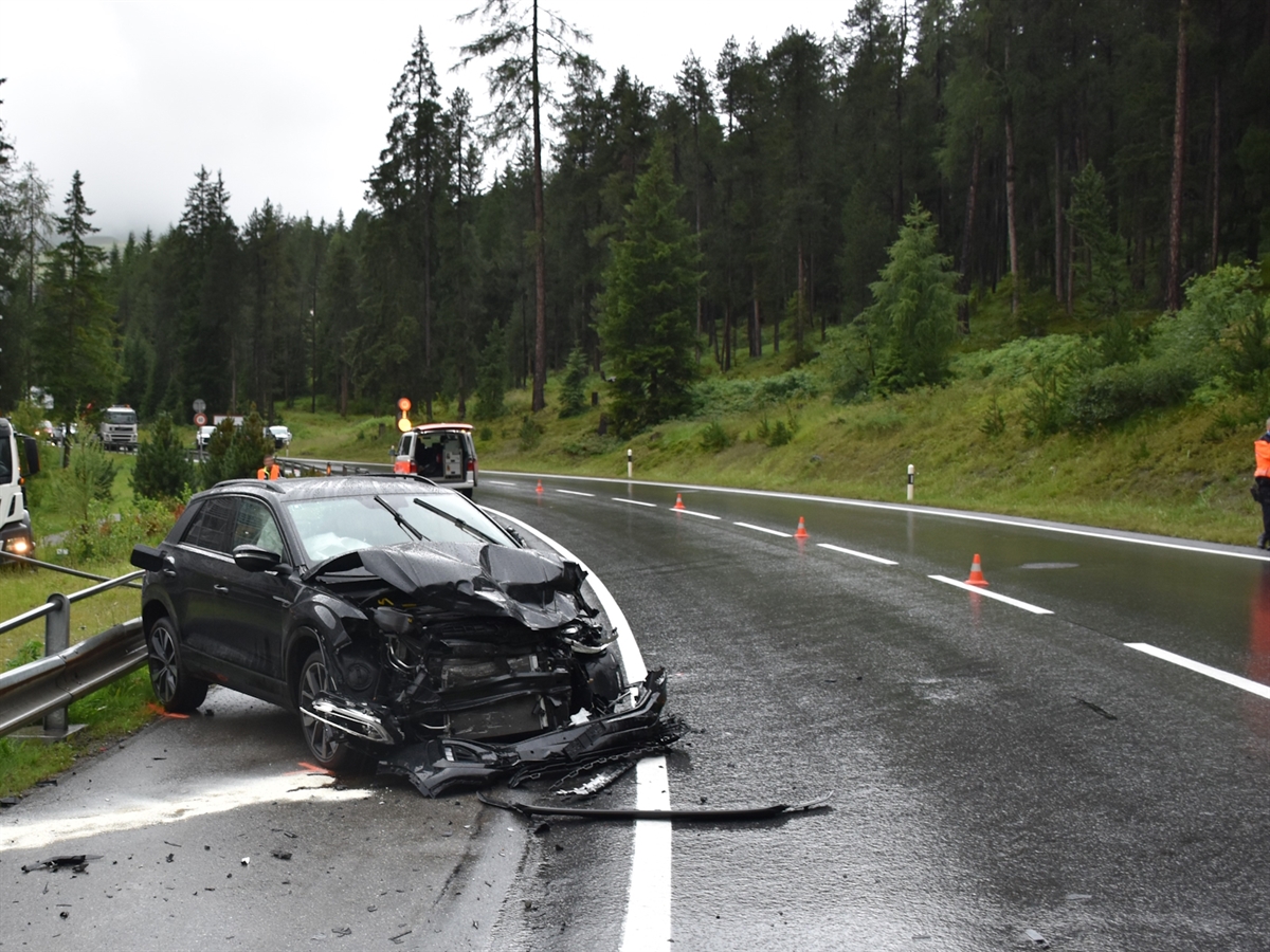 Am Strassenrand das frontal stark beschädigte Auto. Im Hintergrund auf einer Wiese der Lastwagen sowie auf der Strasse ein Polizeiauto.  