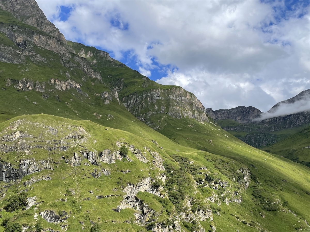 Der Berghang, abgegrenzt durch Horizont und teilweise bewölkten Himmel.