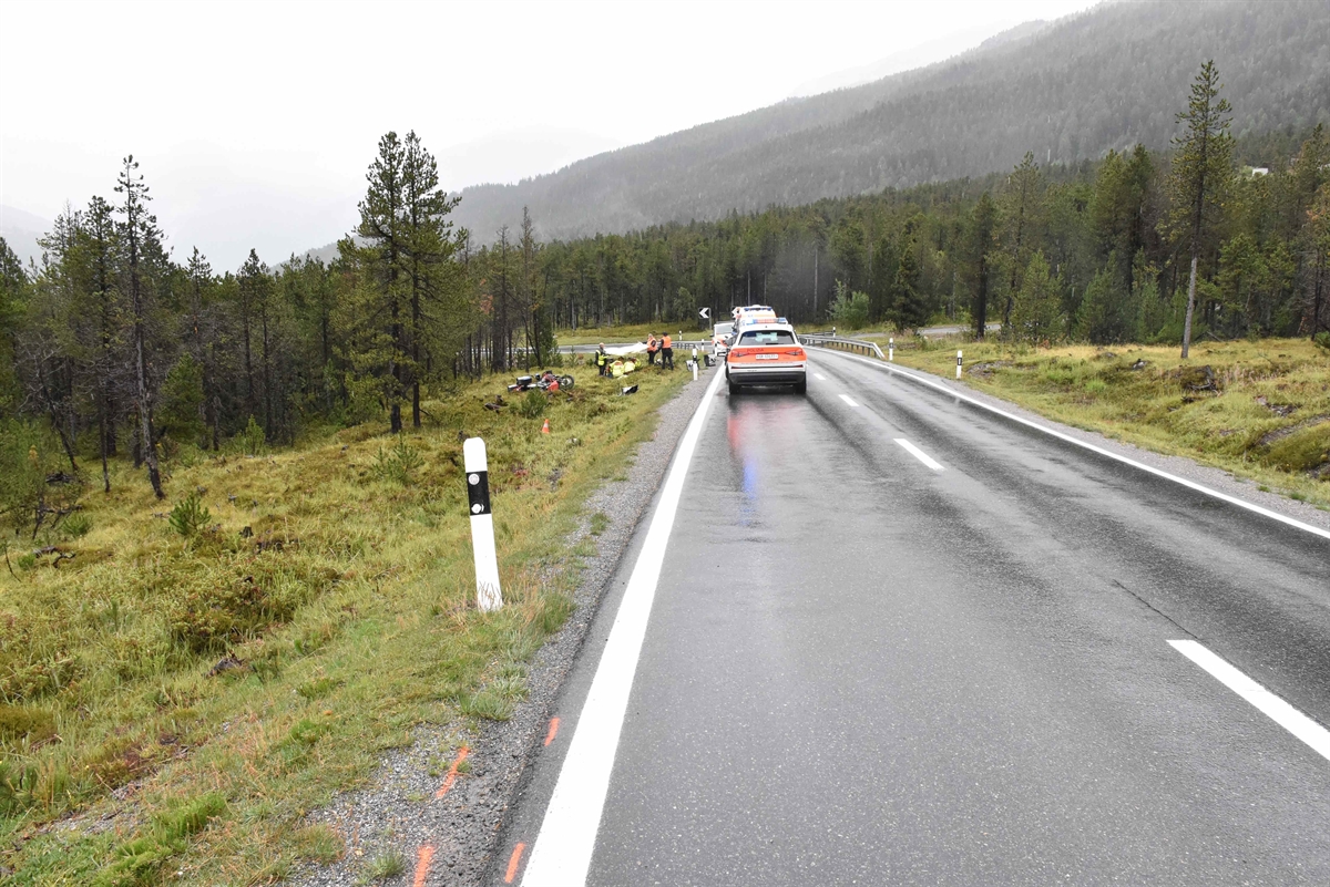 Übersichtaufnahme der Unfallstelle. Es ist ein Polizeifahrzeug zu sehen und auf der linken Seite liegt das Motorrad in der Wiese. Die Einsatzkräfte betreuen den Verunfallten.