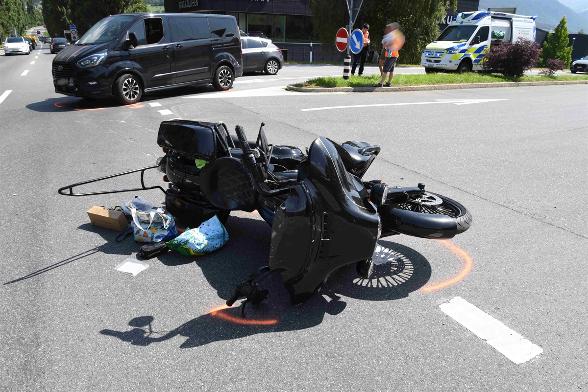 Strassenkreuzung das verunfallte Motorrad schwarz liegt am Boden und im Hintergrund der beteiligte Personenwagen Farbe schwarz und der Krankenwagen. Ein Polizist und zwei Personen in der Grünstreifeninsel mitten der Kreuzung zu sehen.