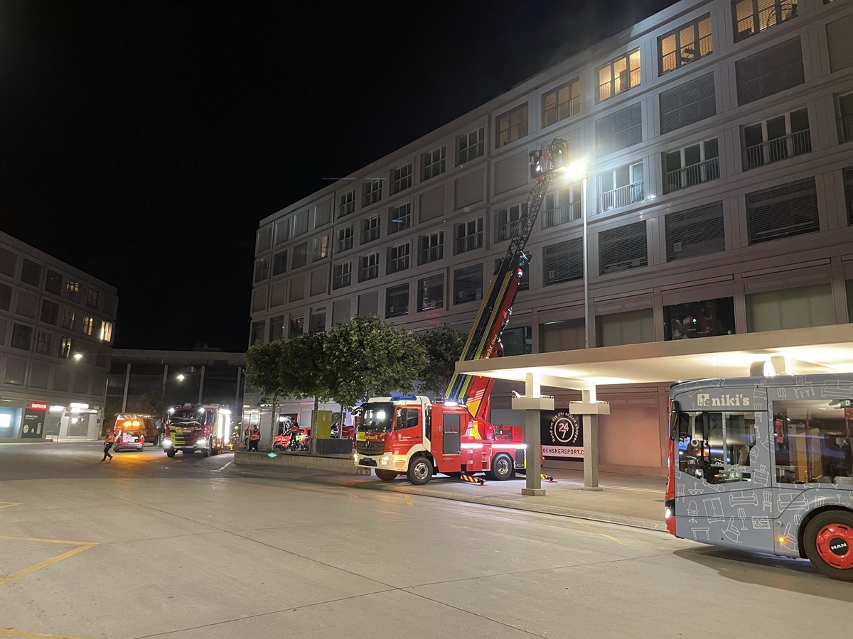 Übersichtsaufnahme des Gewerbegebäude beim Bahnhof in Chur. In der Mitte des Fotos steht der ausgefahrene Hubretter der Feuerwehr mit Feuerwehrleuten im Einsatz. Die Feuerwehr leuchtet mit einem Scheinwerfer ins Gebäude.