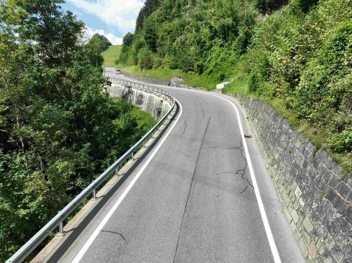Drohnenaufnahme der Strasse einer Geraden und anschliessender links rechts Kombination. Linkseitig Leitplanke und rechts bergseitig die Natursteinmauer.