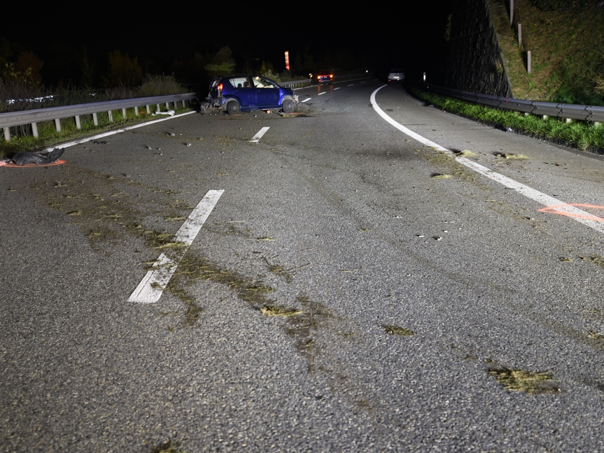 Die mit Gras verschmutzte Fahrbahn der Nordpur. Am oberen Bildrand ein total beschädigtes blaues Auto. Dahinter die beiden anderen beteiligten Autos.