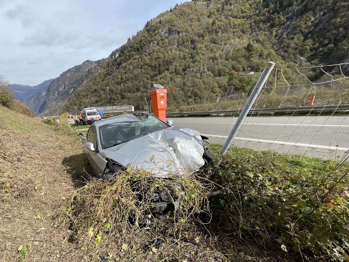 Das total beschädigte Auto in der Wiesenböschung. Das Dach ist auf der Fahrerseite aufgeschlitzt. Im Hintergrund Einsatzfahrzeuge.
