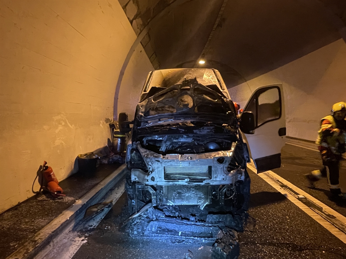 Aufnahme auf die ausgebrannte Front des Lieferwagens. Daneben zwei Einsatzkräfte der Feuerwehr.