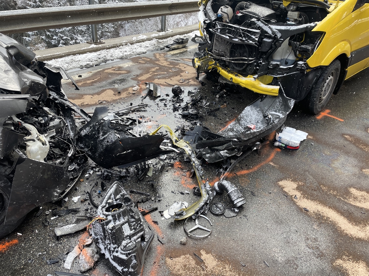 Die beiden Fronten der total demolierten Fahrzeuge. Auf der Fahrbahn liegen Motor- und Fahrzeugteile. Das auslaufende Öl wurde mit speziellem Granulat gebunden