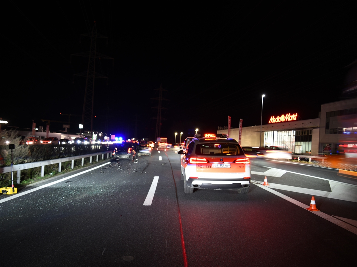 Übersichtsaufnahme in der Nacht mit einem Polizeifahrzeug auf der Normalspur der A13 und den Unfallfahrzeugen auf der Überholspur. Rechts neben dem Polizeiauto die Sperrfläche zu Beginn der Einfahrtspur auf die Autobahn. Blaulicht erhellt die Nacht.