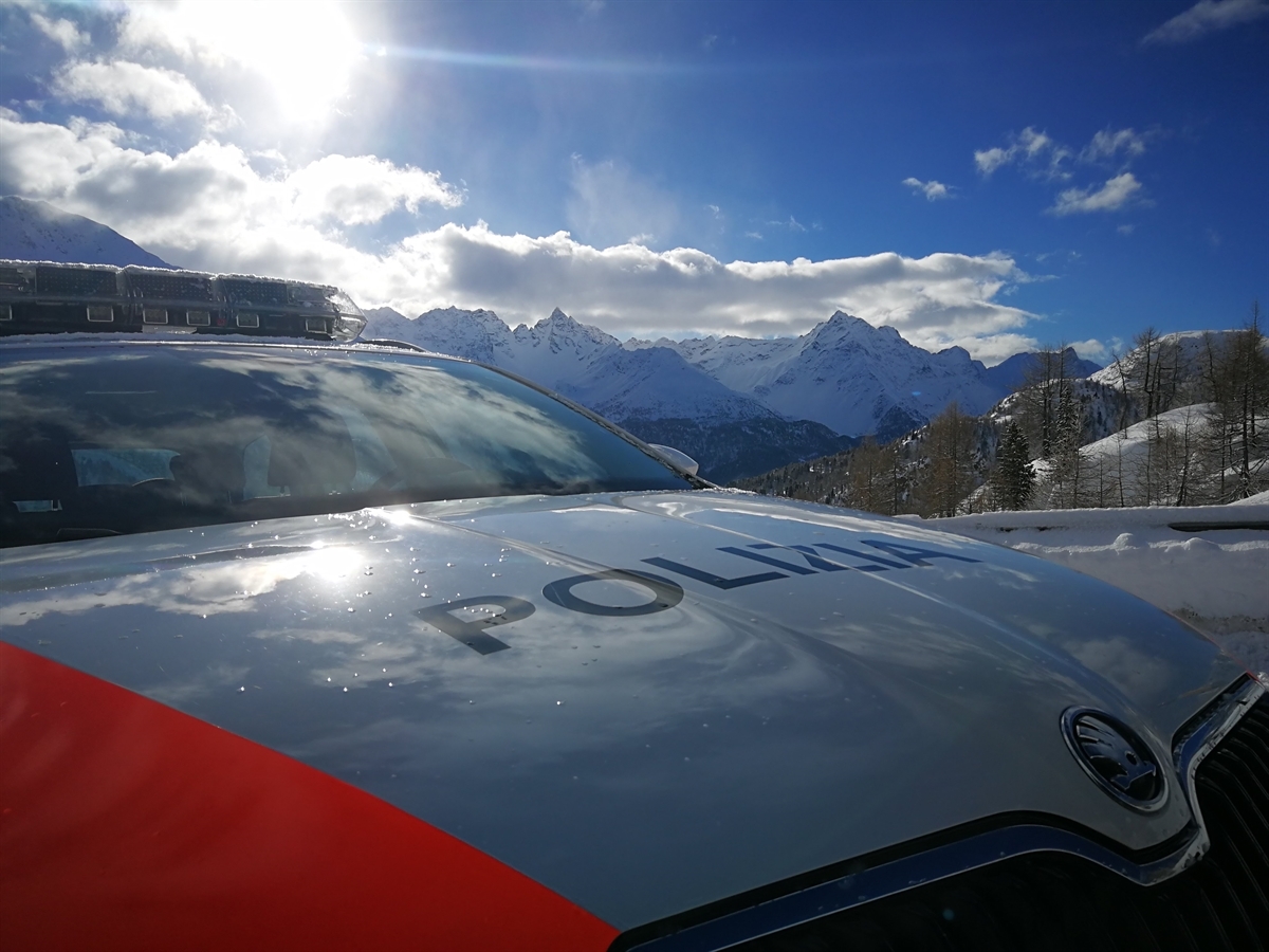 Ein Patrouillenfahrzeug der Kantonspolizei Graubünden vor malerischen, im Winterkleid eingehüllter Bergkulisse.