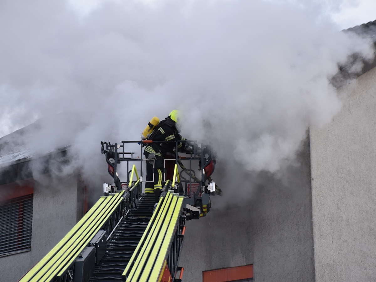 Feuerwehr auf Drehleiter beim Löschen des Brandes. Starke Rauchentwicklung.