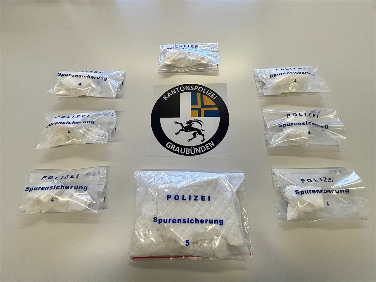 Acht Säckchen mit Kokain abgefüllt auf einem Tisch. In der Mitte das Emblem der Kantonspolizei Graubünden.