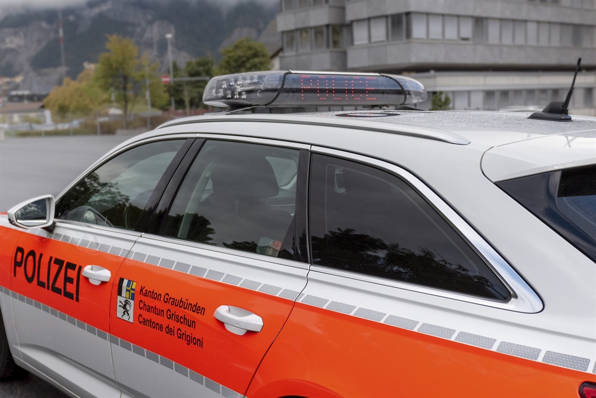 Nahaufnahme einer polizeilichen Anhaltung des Verkehrs. Detailaufnahme der linken Fahrzeugseite eines Patrouillenfahrzeuges. Daneben ein Polizist von hinten gesehen mit Haltezeichen per Hand.
