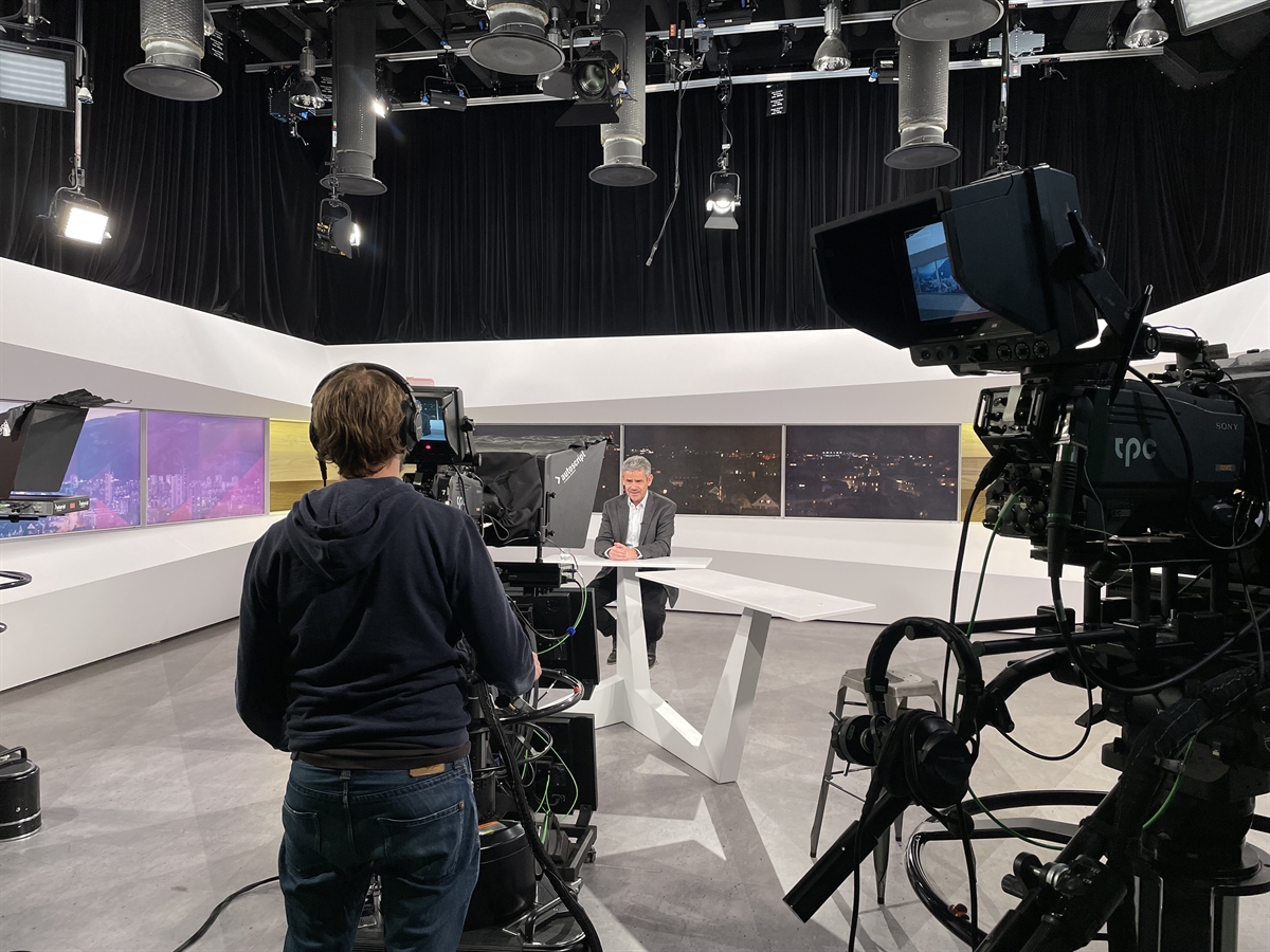 Ein Kameramann von hinten im Studio, etwas weiter entfernt sitzt der Fachmann.