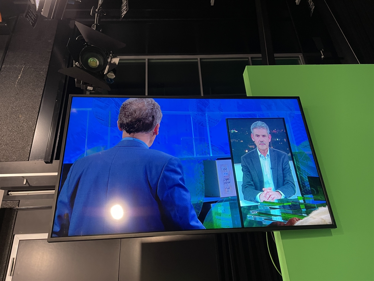 Aufnahme eines Wandbildschirms mit einem Moderator von hinten und dem Fachmann frontal.