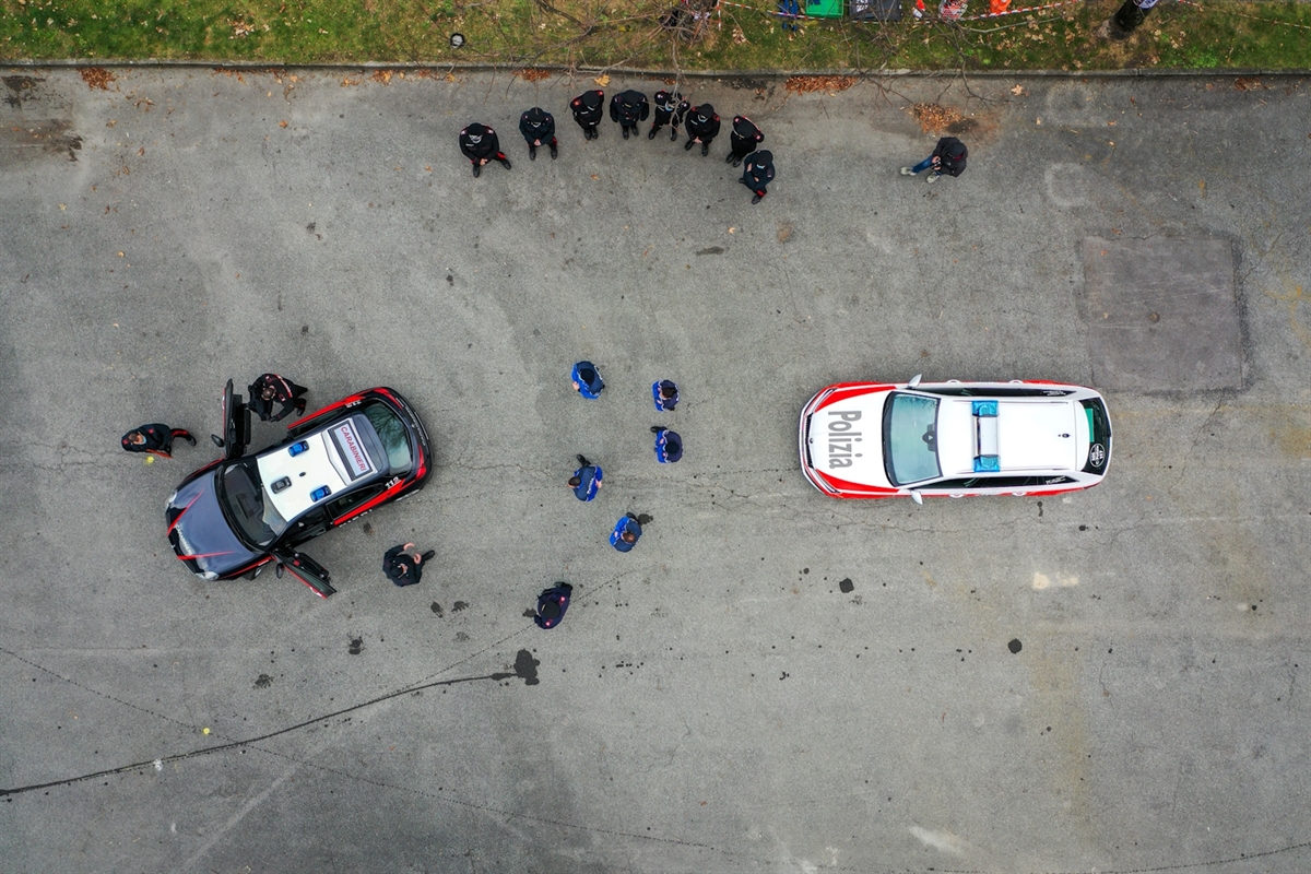 Luftaufnahme auf ein Fahrzeug der Carabinieri und eines der Polizei. Um die Fahrzeuge stehen formierte Einsatzkräfte.