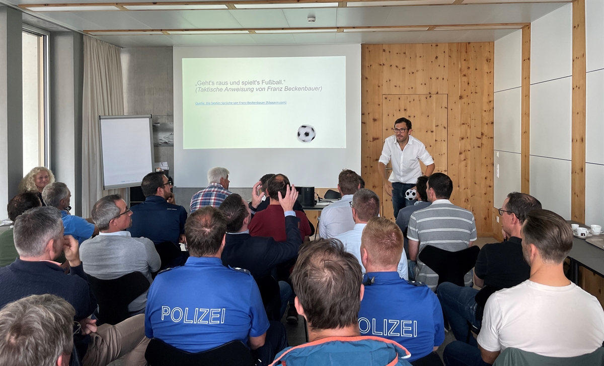 Dozent wirft einen Fussball in die Zuschauerrunde