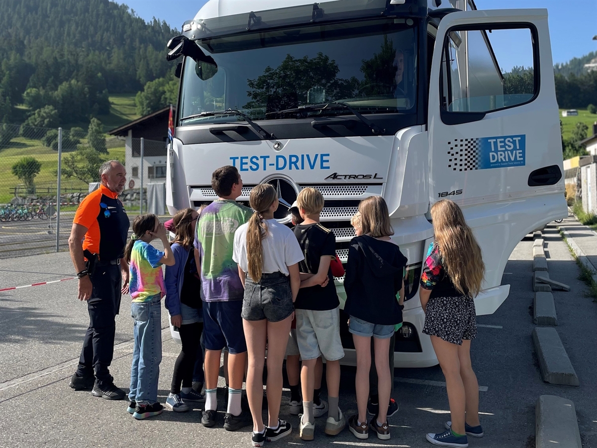 Die Kinder stehen ganz nahe vor dem Lastwagen und ein Kind sitzt in der Führerkabine und erlebt so, wie die Sicht ist.