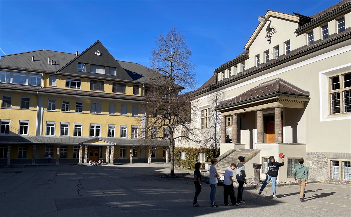 Schulhausgebäude, Kinder spielen Korbball, blauer Himmel