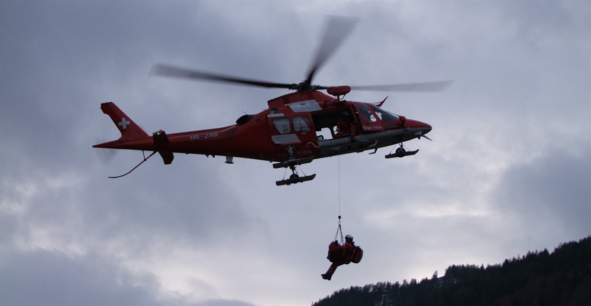 Ein Bild in luftiger höhe. Am Rega-Helikopter hängt an der Winde der Rettungsspezialist Hubschrauber sowie die geborgene Person.