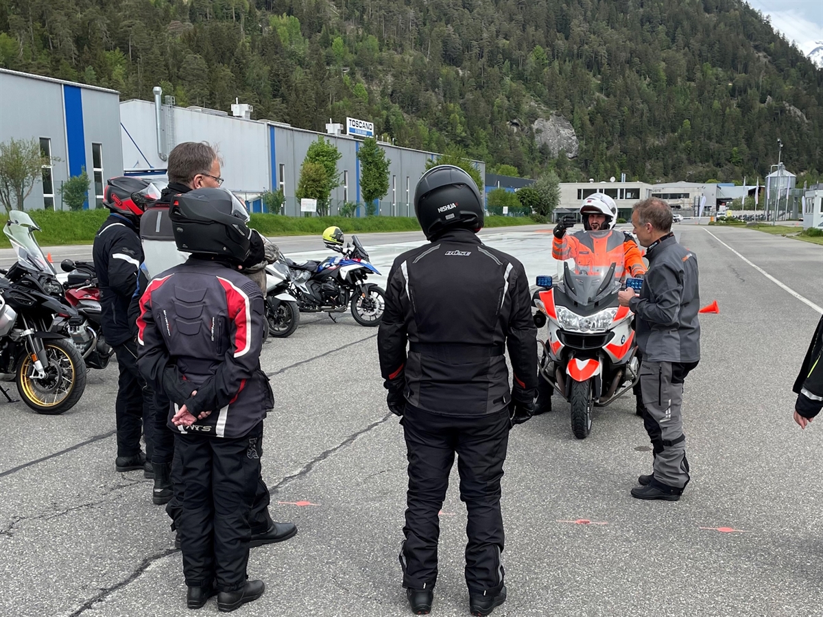 Kursteilnehmende stehen um einen Polizisten auf dem Motorrad. Ein Instruktor gibt Erklärungen ab.